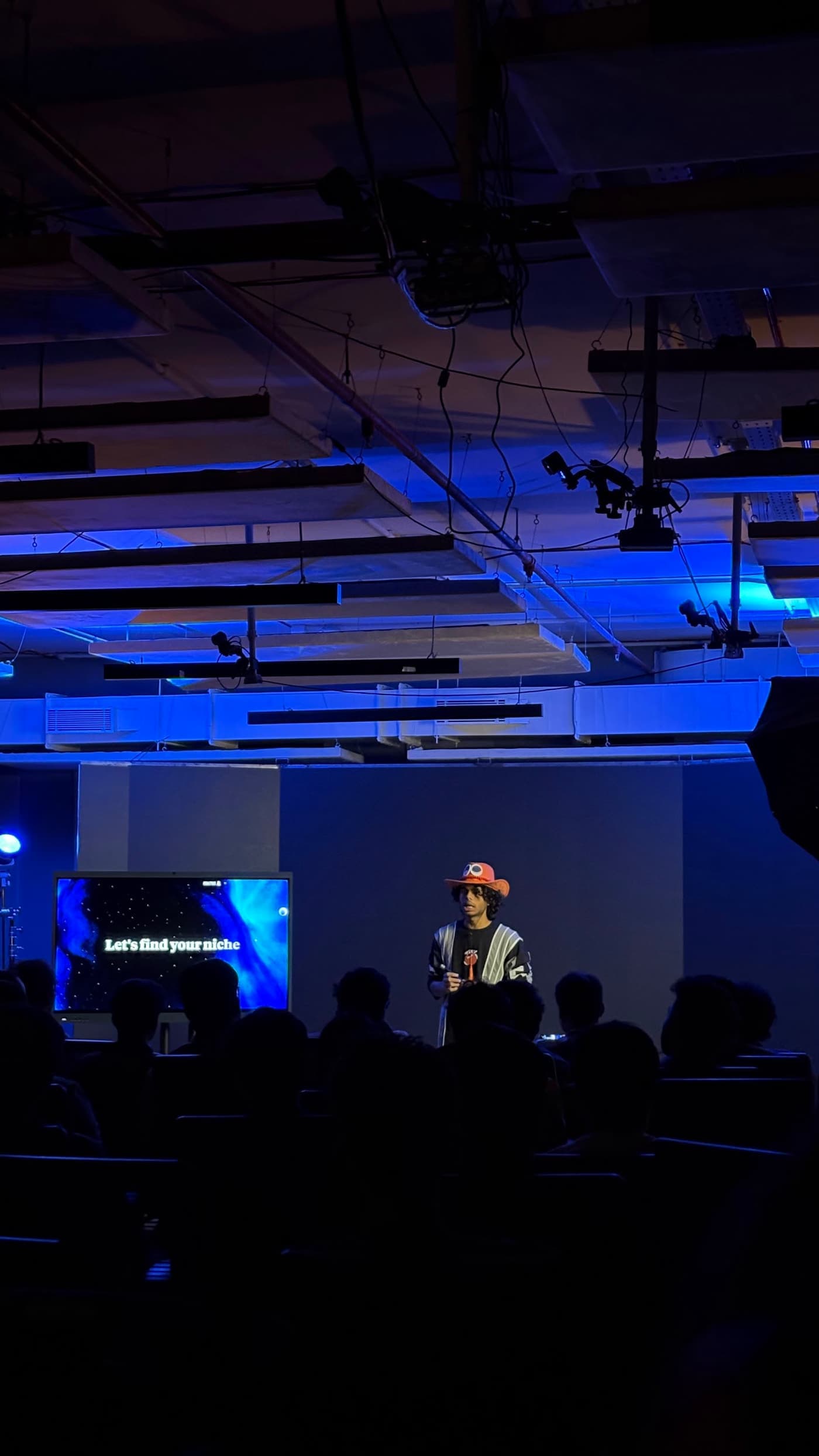 An instructor on the GenC stage beside a screen that reads "Let's find your niche"