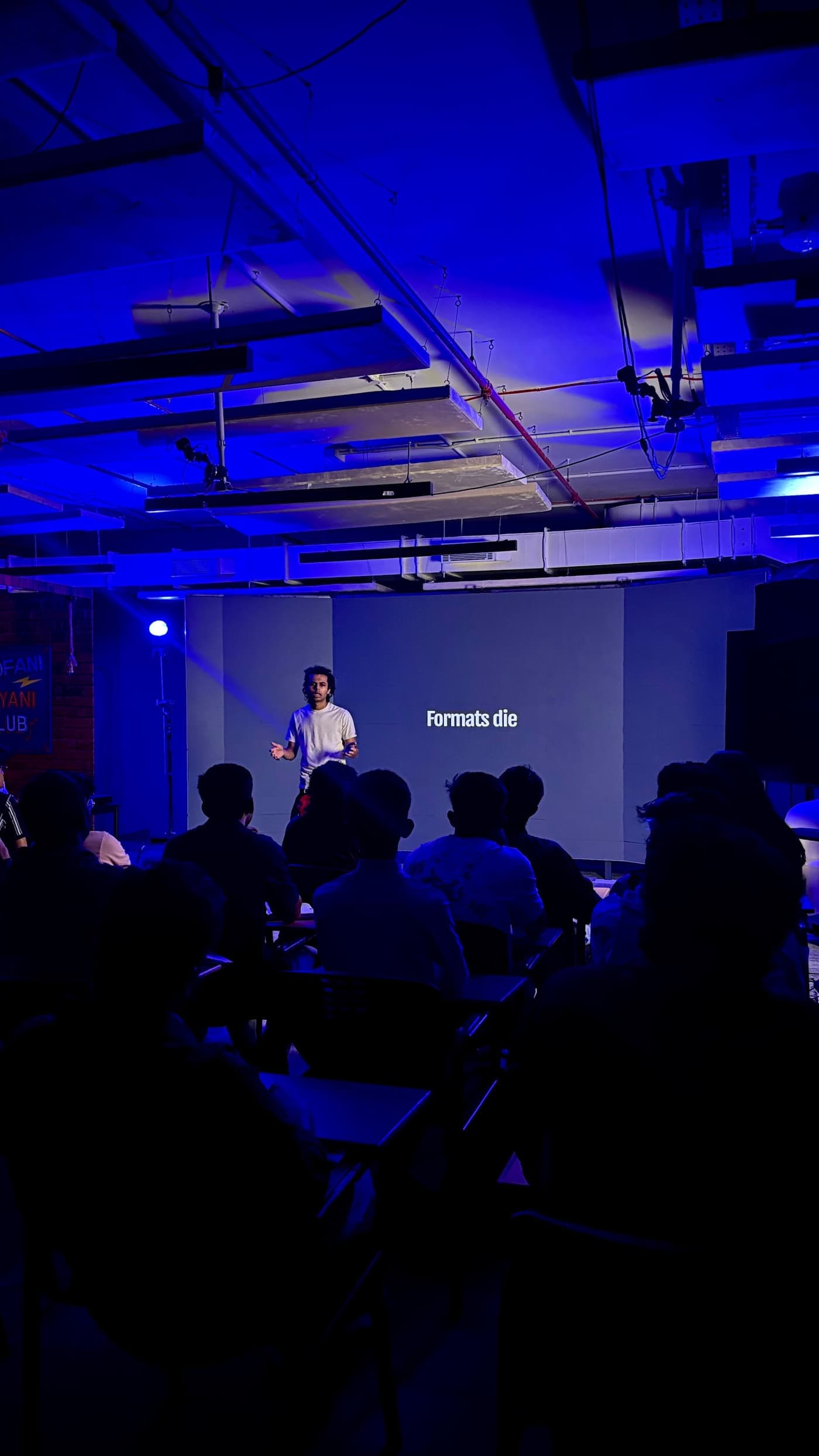 A live class at the GenC studio in Bangalore: an instructor on stage under blue light, the room full of students